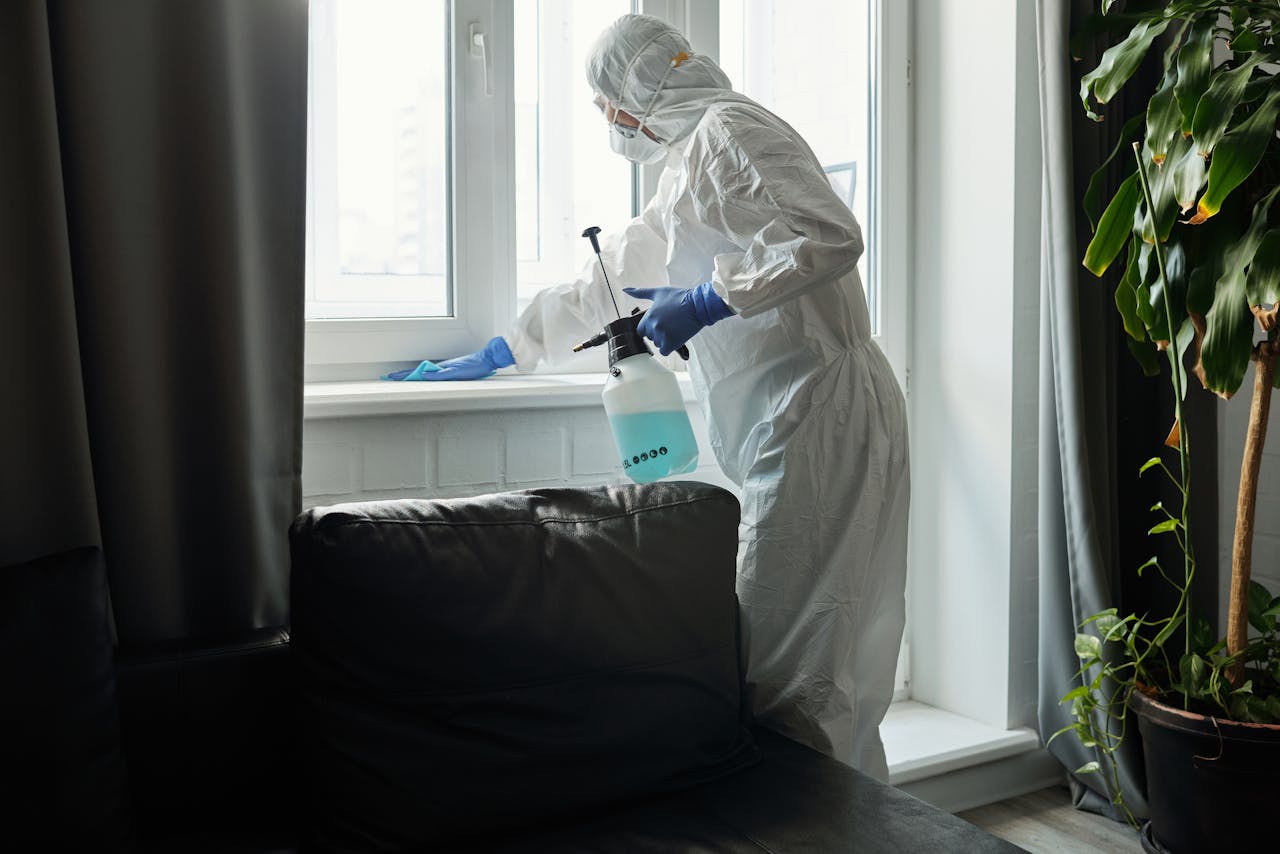 services-01 Person in PPE disinfecting indoor window area during COVID-19 pandemic.