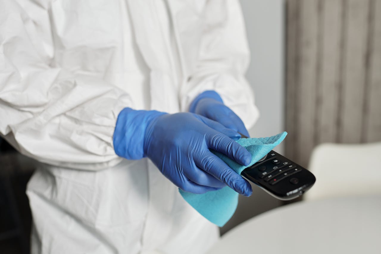 about-01 Close-up of a person disinfecting a remote control wearing protective gloves, ensuring cleanliness.